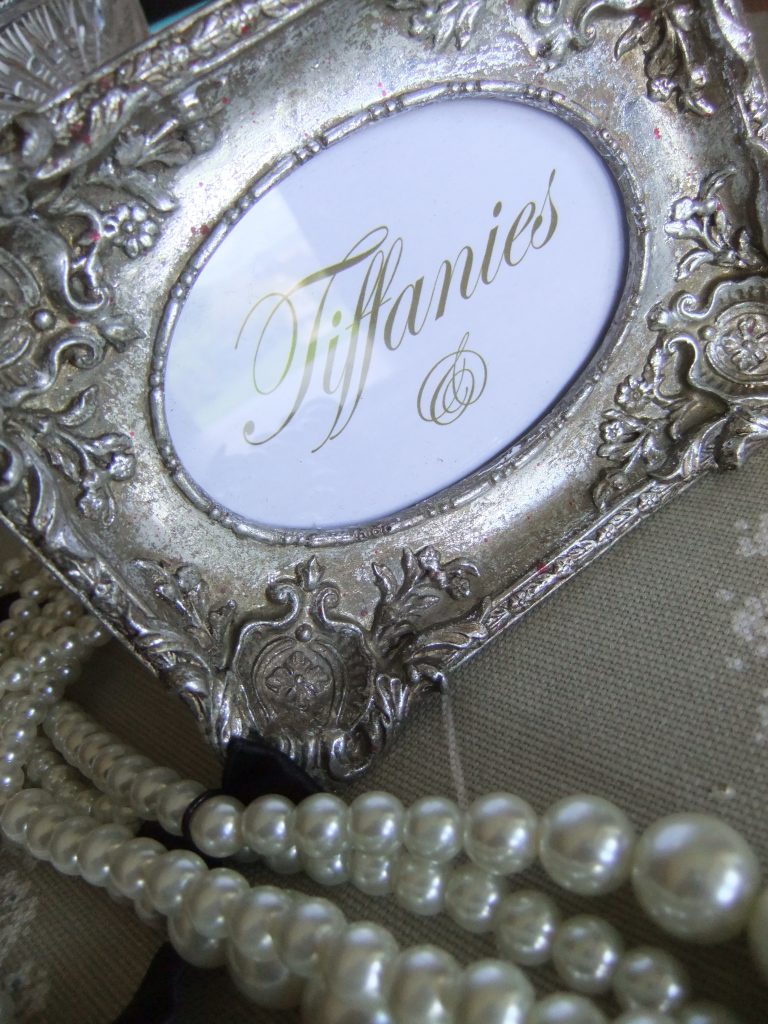Close up Of a silver ornate photo frame with tiffanies in it for a wedding table plan and a string of pearls draped round the frame to hire