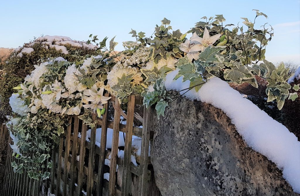 winter flower garland filled with ivy and lilies across a snow covered trellis and Cotswold stone wall can be used as an arrangement for the top table or part of a floral wedding arch