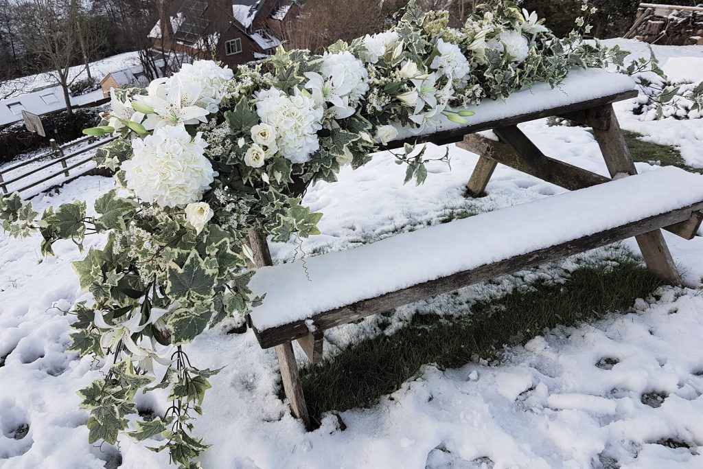 Hire winter white flower garland to dress wedding top table Led across a picnic bench covered in snow with a snowy background of the Cotswold valley