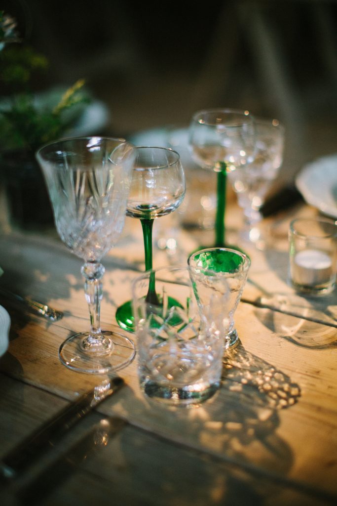 A natural wooden trestle table with vintage cut crystal wine glasses and water tumblers, and a vintage shot glass and green stemmed wine glass available to hire for weddings and events