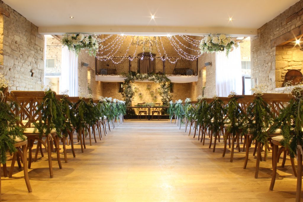 ceremony set up at the great tythe barn in Tetbury with a faux floral arch and fresh greenery for hire