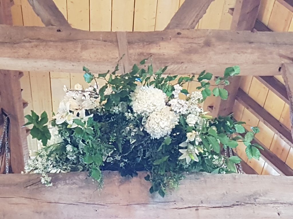 woodland wedding hanging wreath with white and green fake flowers and fresh foliage at Hanley Barn wedding venue available to hire for weddings and events