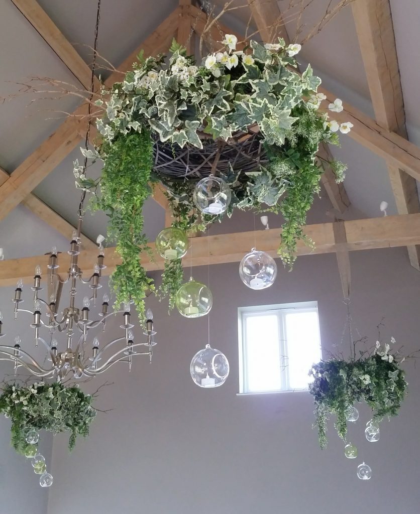 Faux floral and greenery wreaths hanging from the beams at Hyde barn, with glass baubles with tealights in them for hire