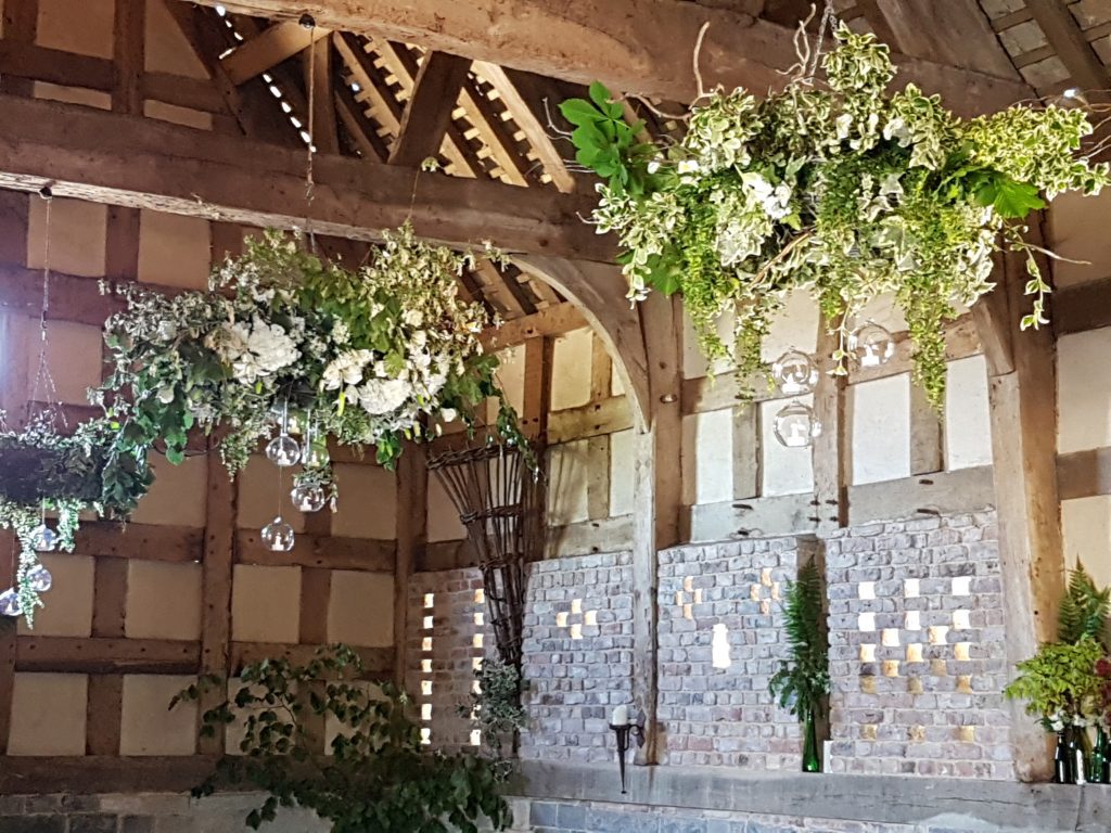 wooden wicker hanging wreath with ivy , faux flowers and glass baubles. green glass bottles in the alcoves around the room all available to hire for wedding and events and film at Frampton Barn wedding venue for hire