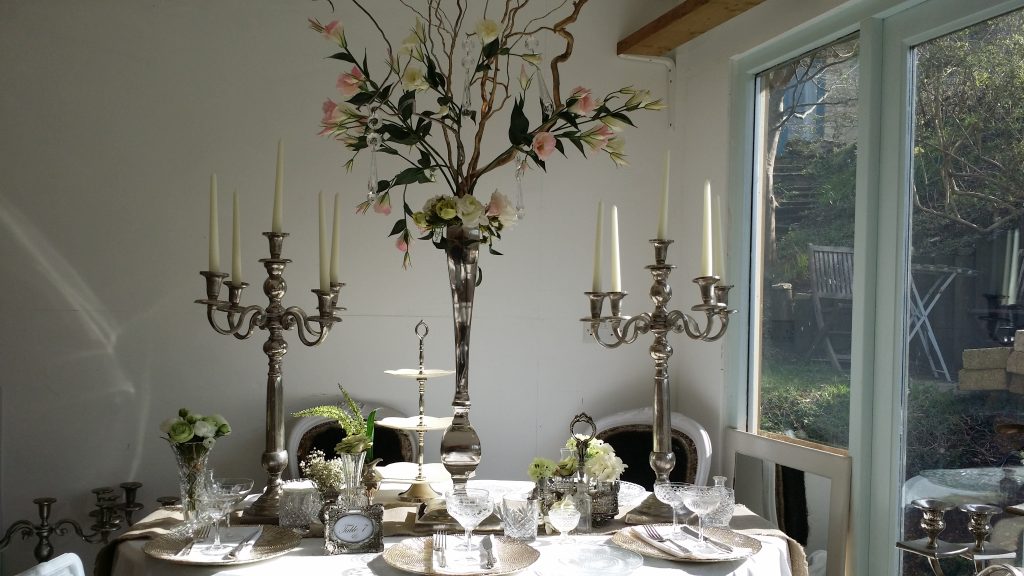 Wedding table dressing for photoshoot with cupcake cake stand silver candelabras and gold charger plates with vintage wine glasses and champagne saucers, silver picture frame table number, and a twisted willow floral arrangement in a silver vase in the centre available to hire