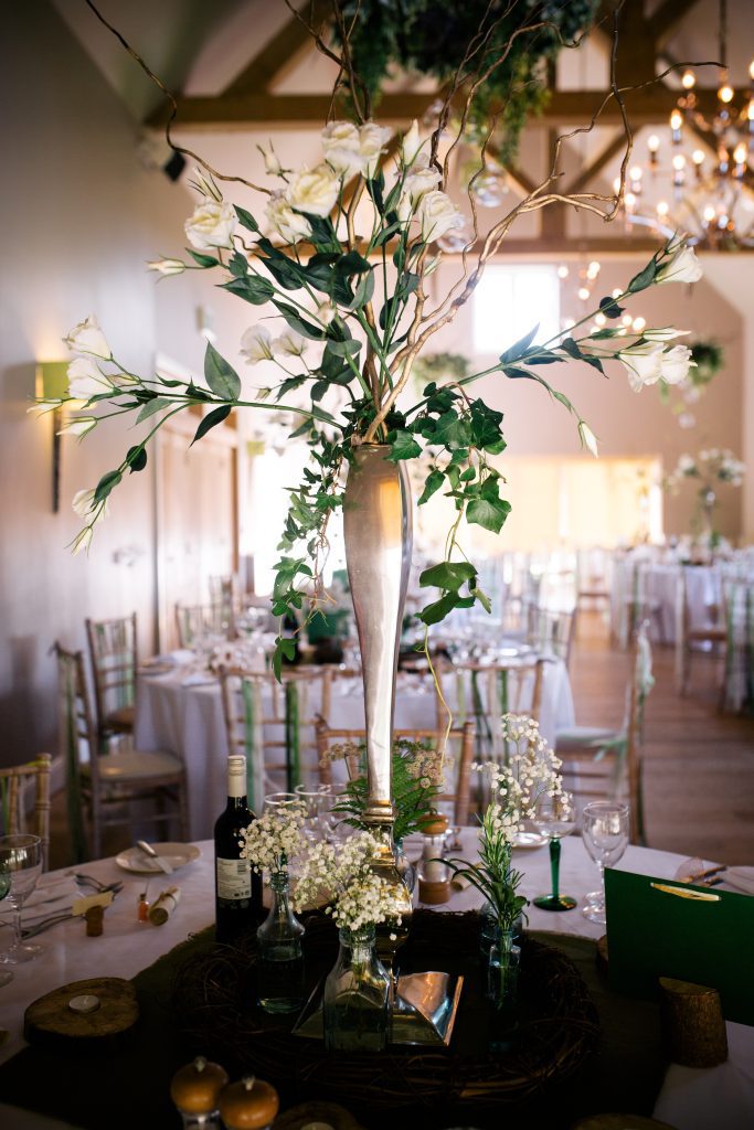 Large lisianthus and twisted willow silver vase centrepiece, with recycled glass bottles and gypsophilia on a log round and log tealight holders to hire