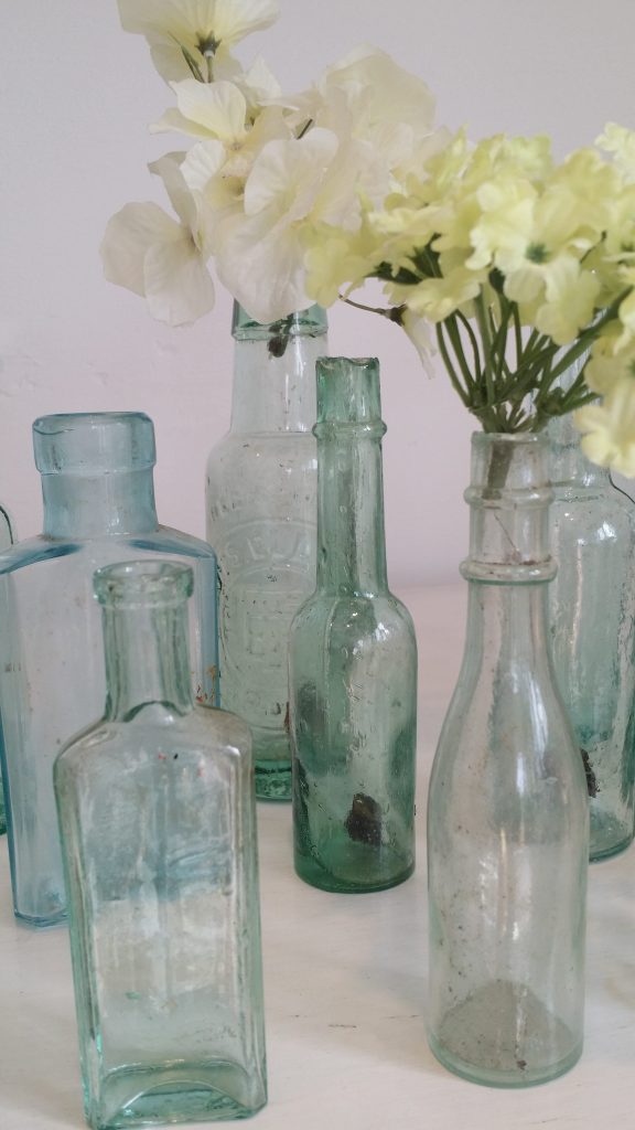 a selection of white, aqua and green recycled glass bottles of different shapes and sizes, with a hydrangea head in two bottles and a white background