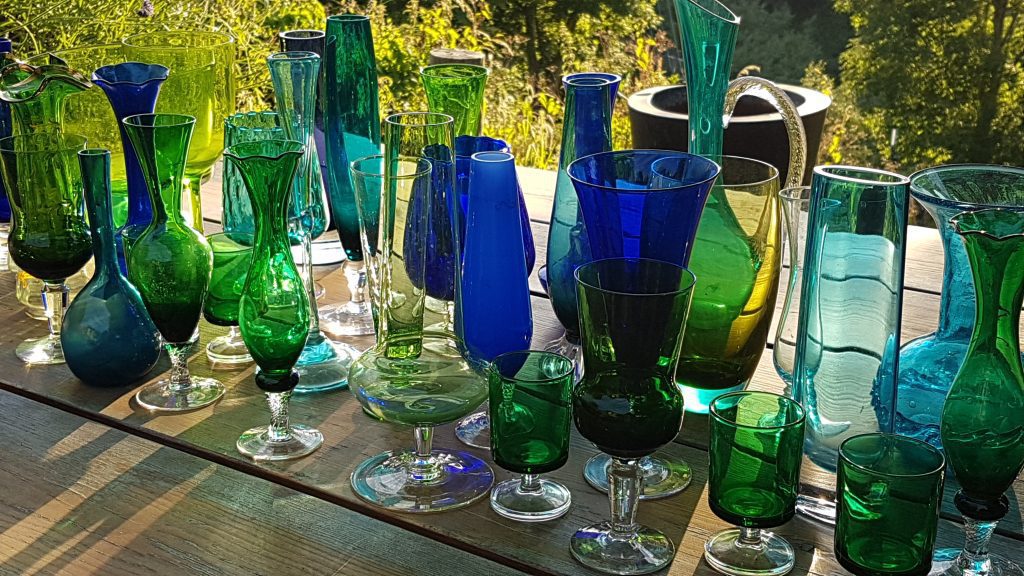 A table set up with blue and green vintage glass coloured vases in different height, style and shapes perfect for flower arrangements for weddings all available to hire