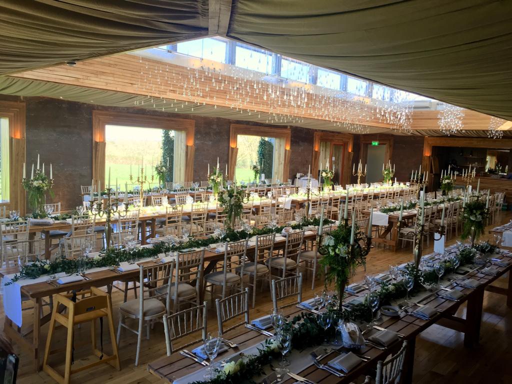 Elmore court in the gilly flower, set up with four rows of trestle with a hessian runner down the middle of each table and filled with gold candelabras with faux flower white and green wreaths and fresh ivy running between each candelabra