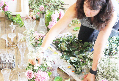 A florist flower arranging using fresh foliage and greenery, with antique pink roses, pink hydrangeas and gypsophila in vintage cut crystal vases and vintage silver cruets sets at the old lodge in Minchinhampton, the Cotswolds
