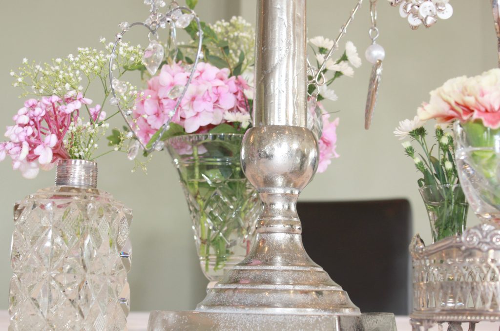 The base of a silver candelabra with hanging hearts surrounded by cut crystal vintage glass vases filled with pink Hydrangeas, pink roses and Gypsophila.