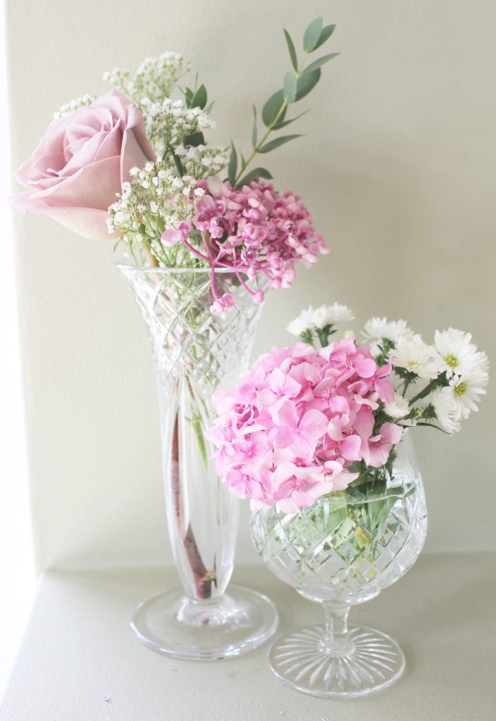 Two vintage cut crystal glass bud vases filled with antique pink roses, pink hydrangea,  white daisies and gypsophila and sprigs of fresh eucalyptus