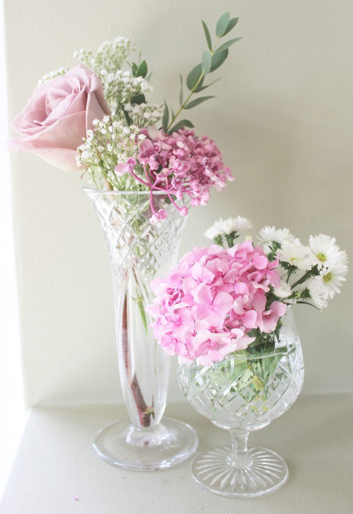 Two vintage cut crystal glass bud vintage vases filled with antique pink roses, pink hydrangea,  white daisies and gypsophila and sprigs of fresh eucalyptus
