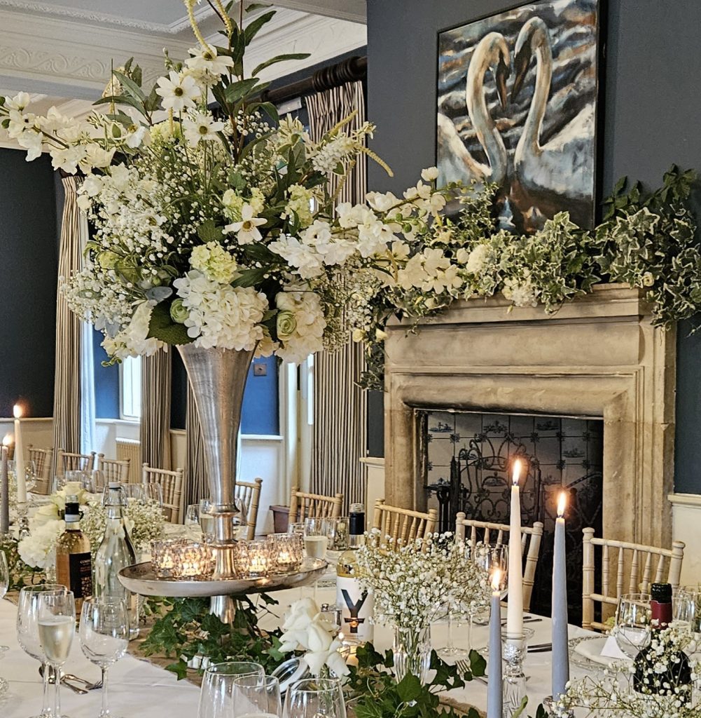 Large silver trumpet vase with tealights around the base and filled with white flowers and greenery available to hire at the swan in bibury