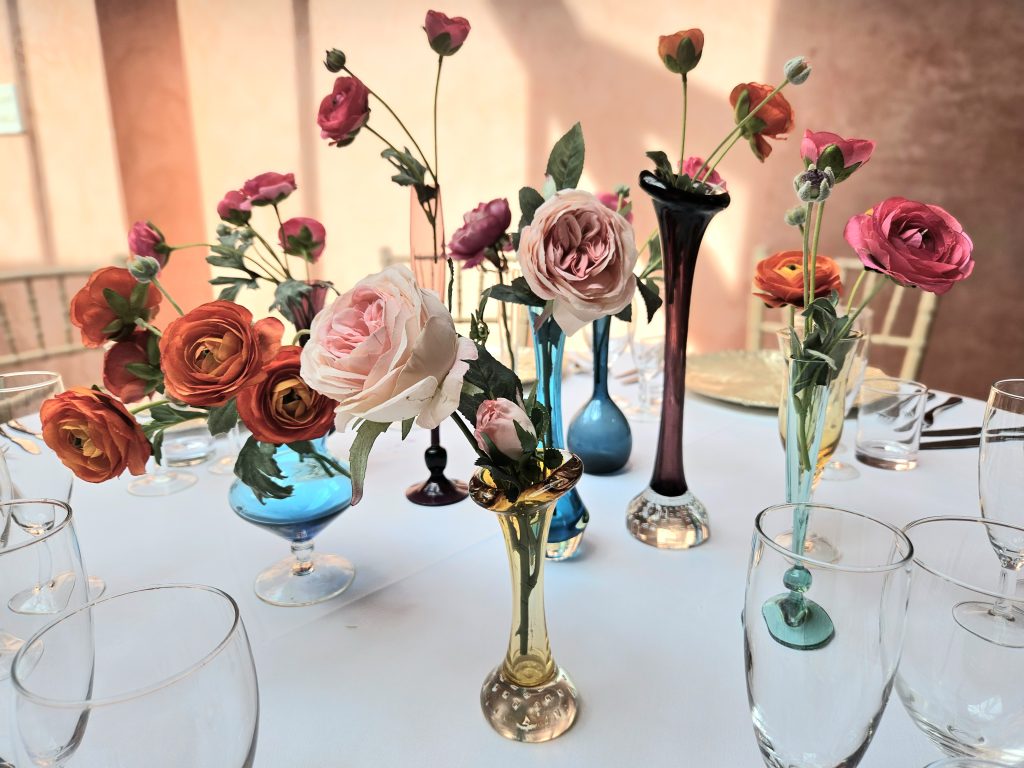 A selection of bright flowers in pinks and oranges in a mixture of coloured glass vases at the Matara