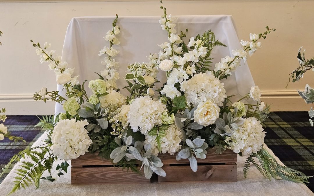 two wooden crates filled with luxury fake flowers in white and green sat side by side at the top of an aisle on a cream carpet runner